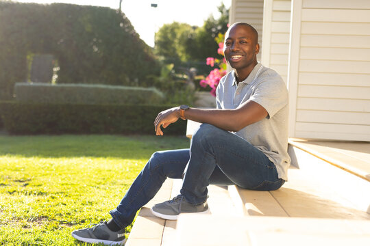 Outdoors, young African American man sitting on porch steps, smiling at camera - Powered by Adobe