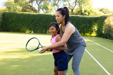 Outdoors biracial mother and daughter teaching tennis on sunny day
