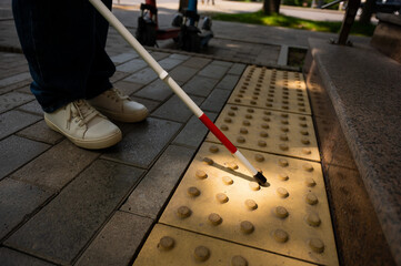 Close-up of female foot, walking stick and tactile tiles. Blind woman climbing stairs using a cane. 
