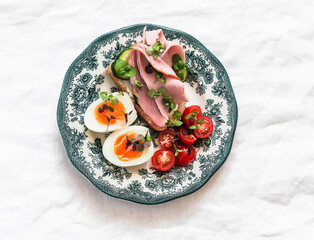 Delicious breakfast, snack - boiled egg, cherry tomatoes, cucumber and ham sandwich on a light background, top view