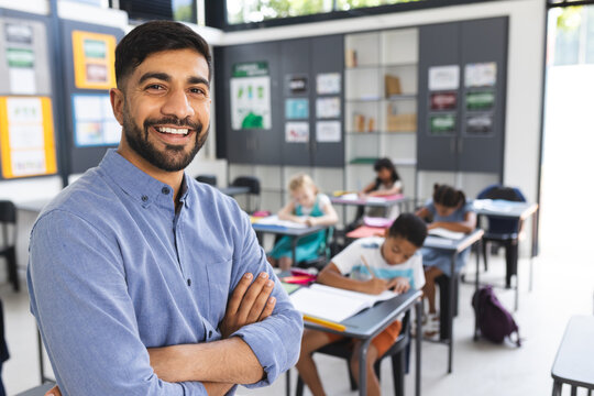 Young Asian male teacher with a beard stands confidently in a school classroom with copy space
