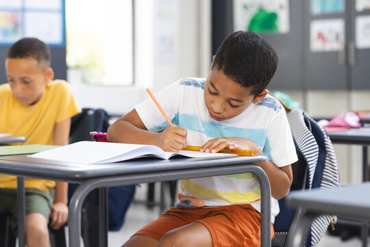 Biracial boy in a striped shirt focuses intently on writing in a school classroom