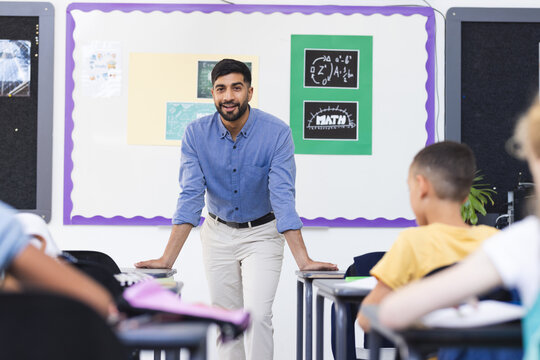 Young Asian male teacher stands confidently at the front of a school classroom