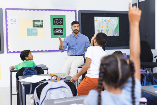 Young Asian male teacher teaching a diverse group of children in a school classroom