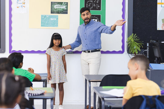 Young Asian male teacher introduces a biracial girl in a school classroom setting