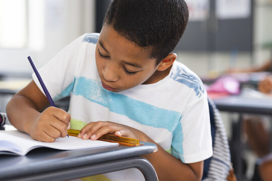 Biracial boy writes in notebook, wearing a striped shirt