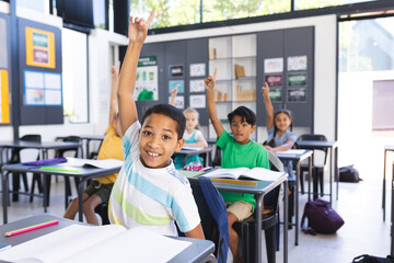 Biracial boy raises his hand eagerly in a classroom