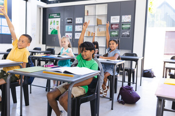 Diverse group of children raising hands eagerly in a school classroom