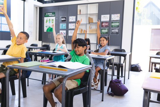 Diverse group of children raising hands eagerly in a school classroom