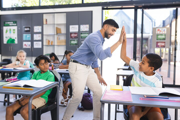 Teacher congratulates a biracial boy with a high-five in a school classroom