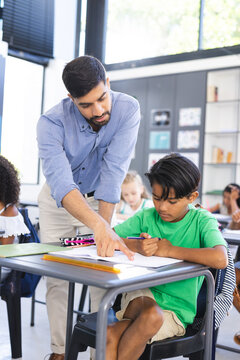 Young Asian male teacher assists a biracial boy in a school classroom