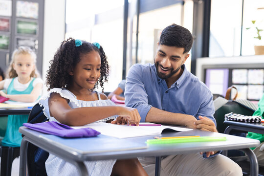 Young Asian male teacher teaching a biracial girl in a school classroom setting