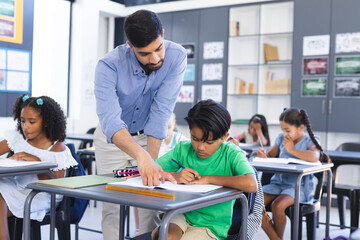 Young Asian male teacher teaching a biracial boy in a school classroom setting