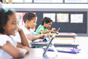 In school, diverse students using tablets and teacher monitoring in the classroom