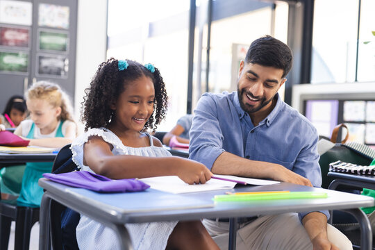 In school, Asian male teacher helping young biracial female student in classroom
