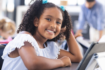 Biracial girl with curly hair and blue hair ties smiles in a school classroom