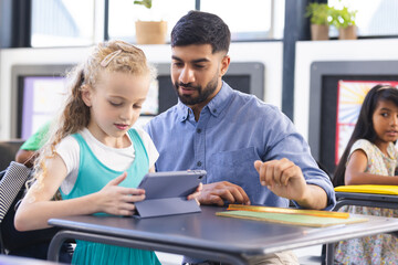 In school, Asian male teacher showing tablet to young Caucasian girl in classroom