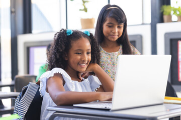 In school, two young biracial female students looking at a laptop screen in the classroom
