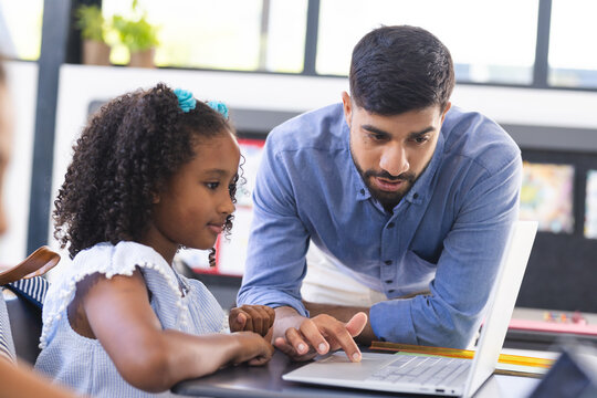 In school, in classroom, Asian male teacher is showing laptop to a young biracial female student