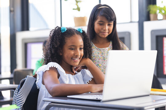 In school, two young biracial female students looking at a laptop screen in the classroom