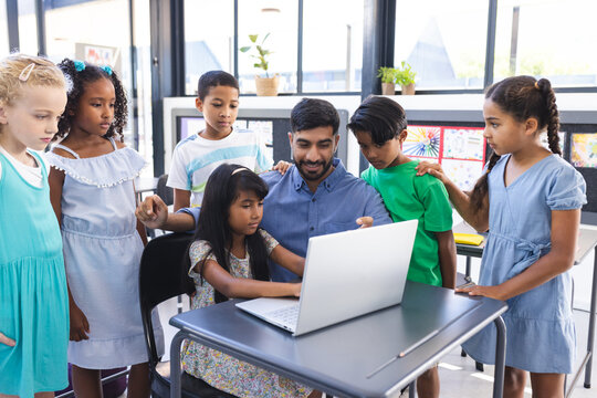 In school, Asian male teacher and diverse students are looking at a laptop in the classroom - Powered by Adobe
