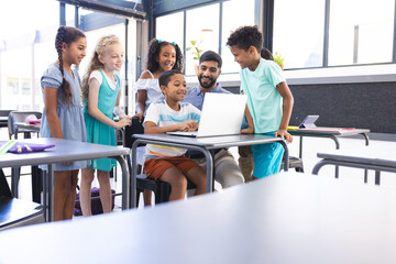 In school, in the classroom, a diverse group of students are surrounding a laptop