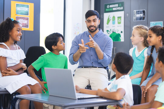 In school, Asian male teacher explaining to diverse group of young students in the classroom