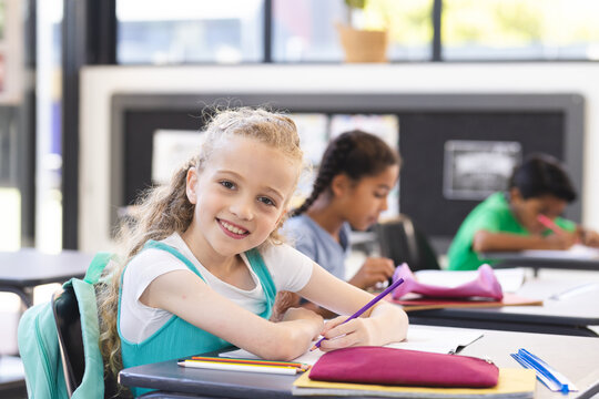 In school, young Caucasian girl wearing light blue top writing in classroom