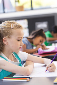 In school, Caucasian girl and her diverse friends focusing on writing in the classroom