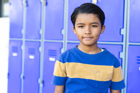 A biracial boy stands confidently in front of blue lockers