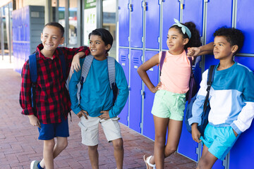 Three biracial boys and a biracial girl stand by lockers in school, smiling