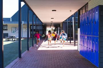 Excited children are running through a school corridor, lockers lining the wall with copy space