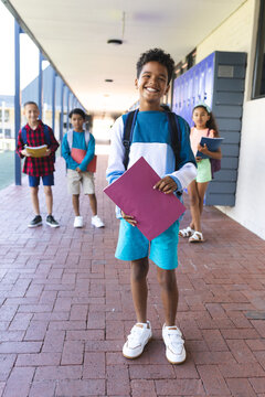 Biracial boy in the foreground smiles, holding a folder, with classmates behind in school