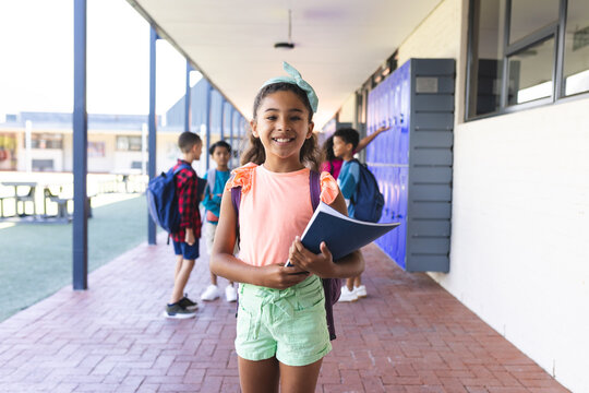 Biracial girl with a blue headband smiles, holding a book at school