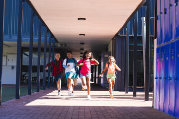 Four biracial children are running joyfully through a school corridor