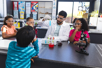 Young Asian male teacher conducts a science experiment for attentive children in school