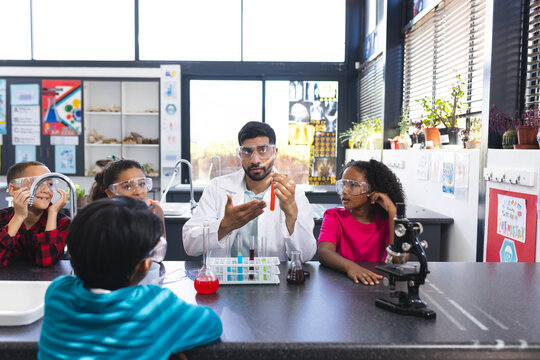 Young Asian male teacher teaches a science lesson to a diverse group of children in school
