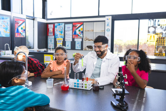 In school, Asian male teacher showing chemistry experiment to diverse students