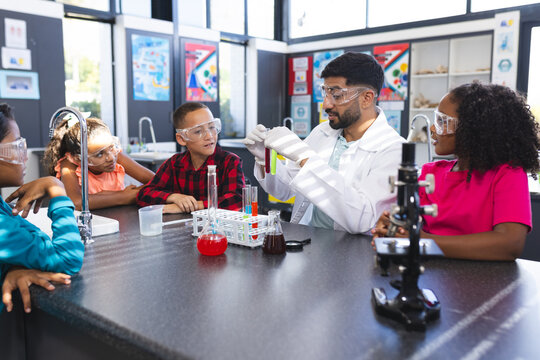 Asian male teacher shows test tube to three biracial students during science experiment