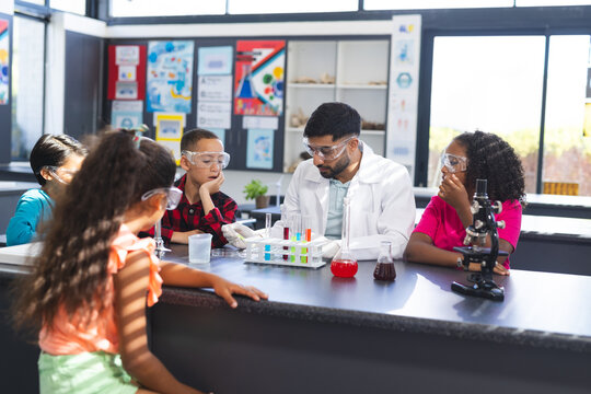 Young Asian male teacher conducts a science experiment with a diverse group of children in school