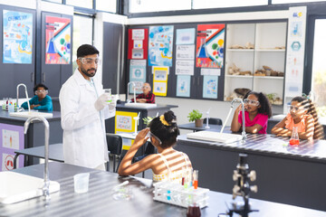 In school, Asian male teacher explaining to diverse students and doing a science experiment