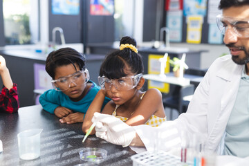 In school, Asian male teacher showing two biracial students science experiment