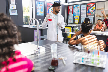 Young Asian male teacher in a lab coat demonstrates a science experiment to students in school