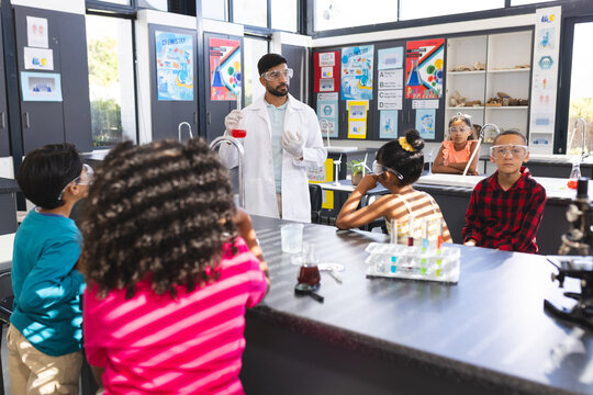 Young Asian male teacher conducts a science experiment for attentive children in school