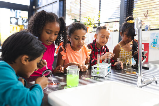 In school, five biracial children are examining science experiments together