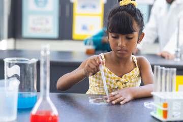 Biracial girl in a yellow dress is conducting a science experiment in school