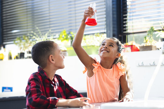 In school, biracial girl and boy are looking at red liquid in flask, doing a science experiment