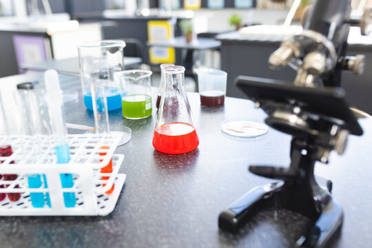 A microscope sits next to colorful liquid-filled beakers and test tubes on a lab bench in school
