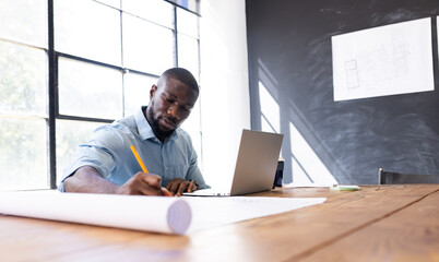 At modern business office, young African American man working on architectural drawings