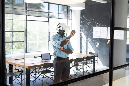 Young African American man in business office using VR headset, engaging with virtual screen